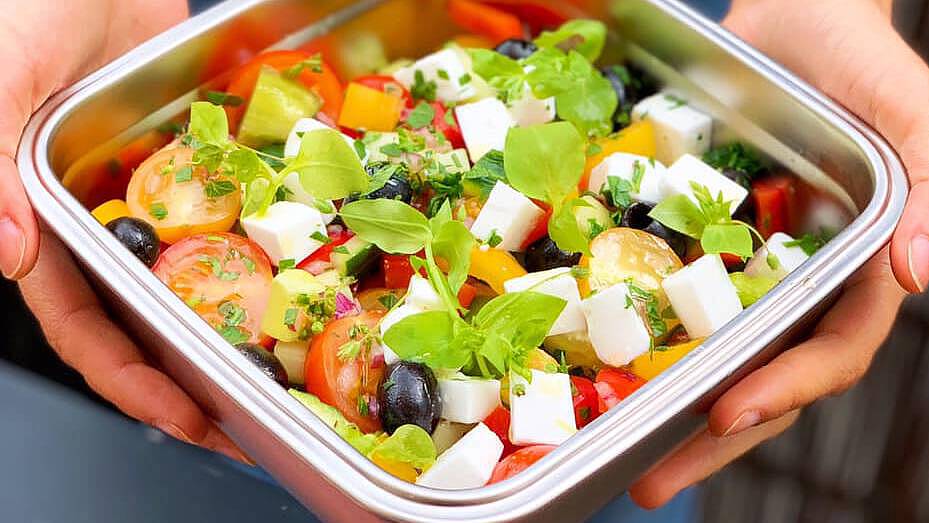 Person holds Greek salad in a metal can