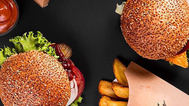 Hamburguesa vegana, papas fritas y salsa de tomate fotografiados desde arriba sobre un fondo negro