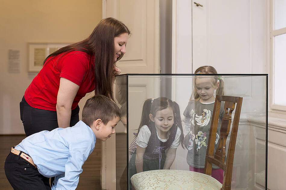 drei Kinder und eine junge Frau schauen sich ein Ausstellungsstück an